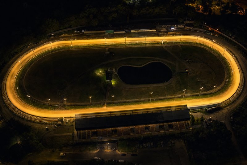 Aerial view of an illuminated greyhound racing oval at night — the setting recreated in free dog racing games